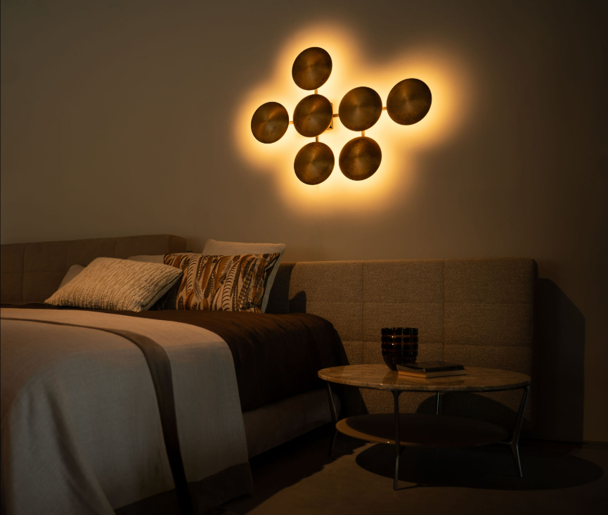 Slaapkamer met beige gestoffeerd hoofdbord, gouden ronde wandlamp met warm licht en een marmeren bijzettafel bij Noort Interieur.